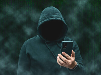 Mysterious faceless hooded anonymous hacker holding smartphone, silhouette of cybercriminal, terrorist.